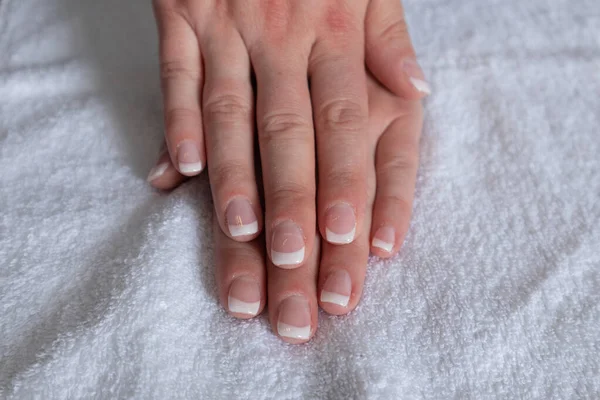 Female hands with french nails polish on a towel in beauty studio. Manicure and beauty concept, close up