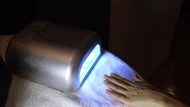 Kobieta wkłada rękę do lampy UV, aby wysuszyć nowy kolor na paznokciach — Wideo stockowe