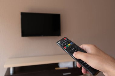 Uzaktan kumandalı bir erkek ve arka planda siyah ekranlı bulanık bir televizyon. Adam TV 'de kanal değiştiriyor. Tasarım için alanı kopyala, kapat, seçici odak