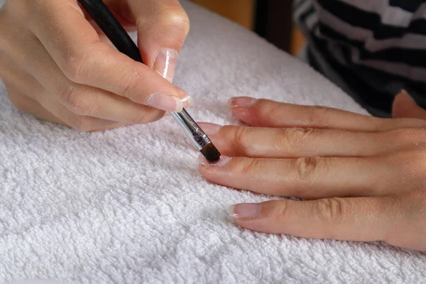 Woman applying protective gel nails polish on a finger on a white towel at home. Beauty and manicure concept. Copy space for design, close up, selective focus
