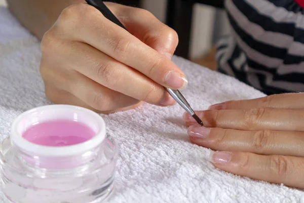 Woman applying pink gel nails polish on a finger on a white towel at home. Beauty and manicure concept. Copy space for design, close up, selective focus