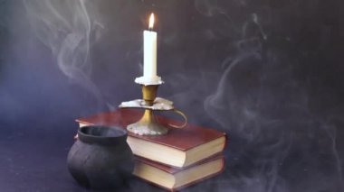 Mumların içinde mum eski kitaplar ve dumanlı çömlek üzerinde yanıyor. 