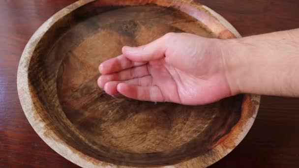 De man steekt zijn hand in een houten kom water en grijpt het water in zijn vuisten — Stockvideo