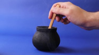 Siyah cadı esrarı tüttürüyor ve koyu mavi arka planda ahşap kaşık karışımları var.