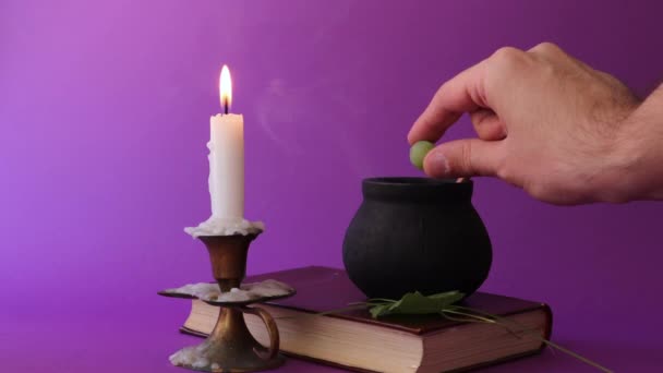 Witch pot is roken op oude boek en hand voegt magische ingrediënten en mengen met een houten lepel, en een kaars in kandelaar branden — Stockvideo