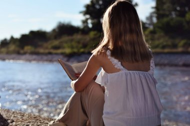 Nehrin kenarında oturan ve bir yaz günü gün batımında kitap okuyan bir kız. Doğa konseptinde rahatlama