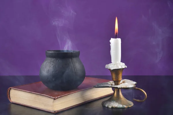 黒の机の上でろうそくの火を灯し 紫色の背景の古い本の上でスモーキーな鍋を切り替える ハロウィンのコンセプト — ストック写真