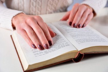 Kadın eli açık bir kitap ve kahverengi ojeli parmaklar üzerinde. Manikür ve güzellik konsepti