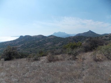 Mavi gökyüzüne karşı uzak dağların ve denizin manzarası.