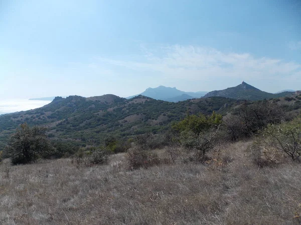 Mavi gökyüzüne karşı uzak dağların ve denizin manzarası.