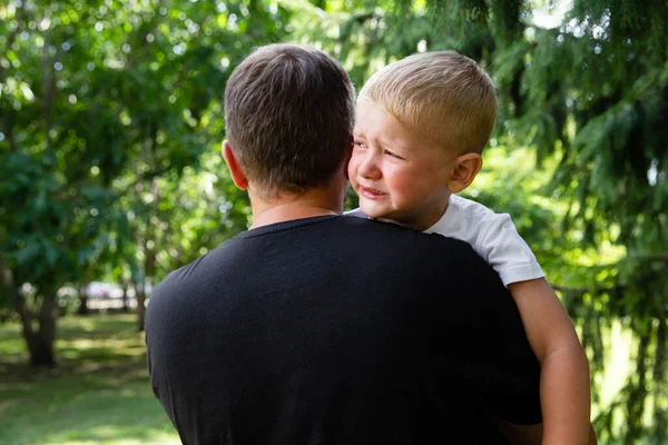 Smutny młody chłopiec płacze na ojcach ręce w przyrodzie, parku, na świeżym powietrzu. Mężczyźni trzymają jego syna, uściski i wygody. Miłość rodzinna, opieka i moralne wsparcie — Zdjęcie stockowe