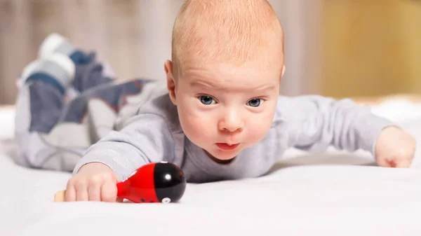 Niño recién nacido sonríe acostado boca abajo con un juguete sobre fondo blanco en el interior. Feliz, lindo y bonito. Cuidado en el hogar y acogedor. Maternidad — Foto de Stock