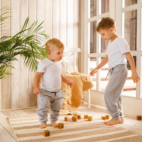 Due fratelli ragazzi che intrecciano con blocchi di cubo di legno sul tappeto lavorato a maglia sul pavimento al coperto. Stile lavorato a maglia all'interno: plaid e moquette. Caldo e accogliente. Bambini giocosi — Foto Stock