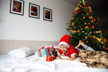 Kapalı alanda Noel etkinliği: Yeni yılın çevrimiçi selamlaşmaları ve toplantıları. Kırmızı Noel Baba şapkalı çocuk tablete bakar ve büyükanne ve büyükbabasıyla iletişim kurar. Tatilin beklentisi.