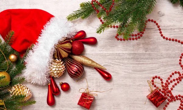 Noel Baba şapkası ve noel süsleri: koni, toplar, bant, boncuklar, hediye kutusu ve ahşap zemin üzerinde Noel ağacı. Kopyalama. Yeni yılın en üst görünümü.