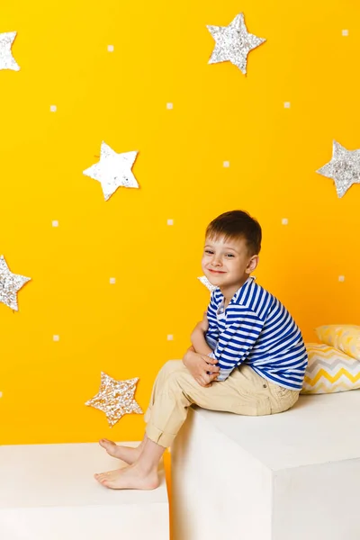 Niño sentado en un cubo blanco sobre fondo amarillo con estrellas —  Fotos de Stock