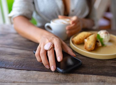 Gül kuvars yüzüklü kız elinde bir fincan kapuçino kahve tutuyor ve telefonu eline alıyor.