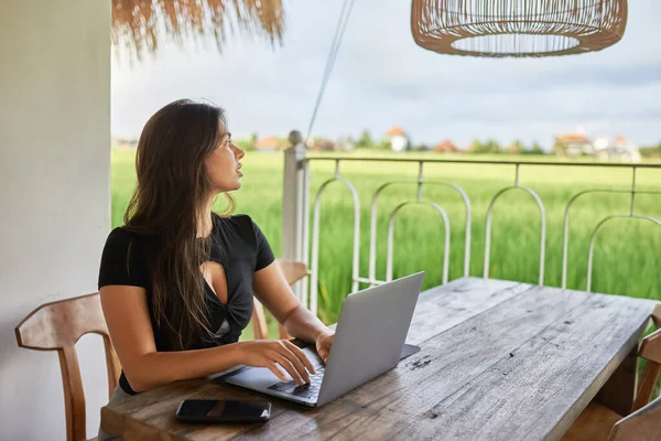 A young girl sits in a cafe with a laptop on a background of green grass.