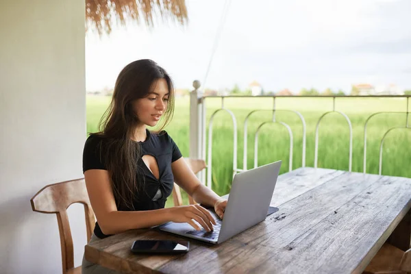 A young girl sits in a cafe with a laptop on a background of green grass.