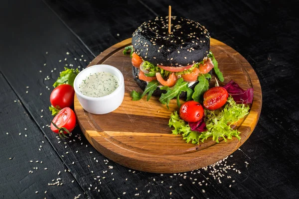Tasty black burger with salmon on wooden background