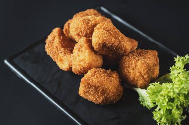 Siyah arka plan üzerine soslu kızarmış balık parçaları. Kopya alanı