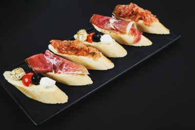 Siyah arka plan üzerine küçük tekne şeklinde jambon ile lezzetli aperatifler. Kopya alanı