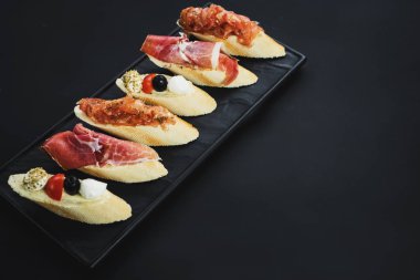 Siyah arka plan üzerine küçük tekne şeklinde jambon ile lezzetli aperatifler. Kopya alanı
