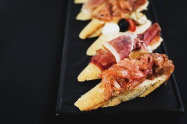 Siyah arka plan üzerine küçük tekne şeklinde jambon ile lezzetli aperatifler. Kopya alanı
