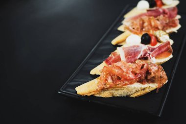 Siyah arka plan üzerine küçük tekne şeklinde jambon ile lezzetli aperatifler. Kopya alanı