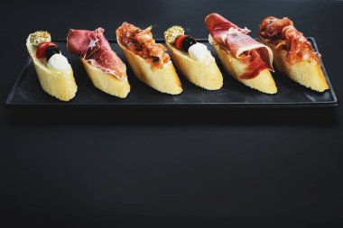 Siyah arka plan üzerine küçük tekne şeklinde jambon ile lezzetli aperatifler. Kopya alanı