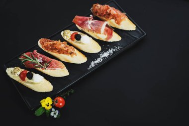Siyah arka plan üzerine küçük tekne şeklinde jambon ile lezzetli aperatifler. Kopya alanı
