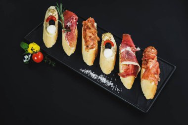 Siyah arka plan üzerine küçük tekne şeklinde jambon ile lezzetli aperatifler. Kopya alanı