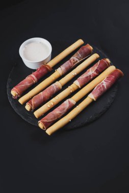 Siyah arka plan üzerine jambon tarafından sarılmış ekmek sopa