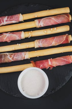 Siyah arka plan üzerine jambon tarafından sarılmış ekmek sopa