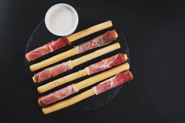 Siyah arka plan üzerine jambon tarafından sarılmış ekmek sopa