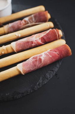 Siyah arka plan üzerine jambon tarafından sarılmış ekmek sopa