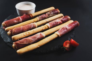 Siyah arka plan üzerine jambon tarafından sarılmış ekmek sopa