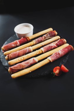 Siyah arka plan üzerine jambon tarafından sarılmış ekmek sopa