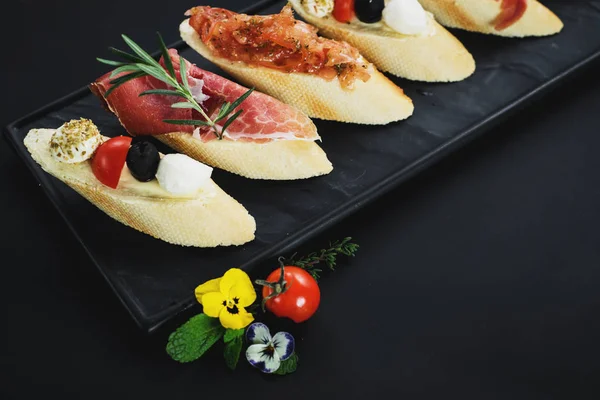 Siyah arka plan üzerine küçük tekne şeklinde jambon ile lezzetli aperatifler. Kopya alanı