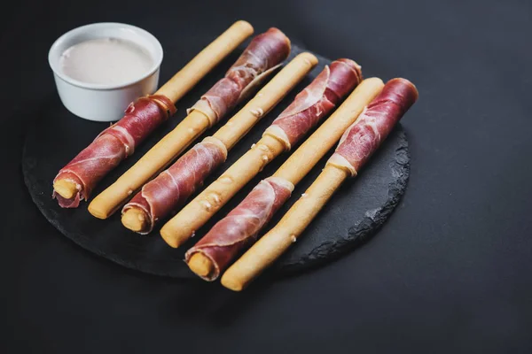 Bread sticks wrapped up by ham on black background