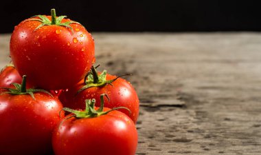 Tahta zemin üzerinde su damlaları olan taze kırmızı domatesler.