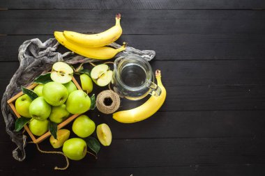 Siyah ahşap zemin üzerinde elma ve muz olan cam bir kavanoz tatlı su. Uzayı kopyala Sağlıklı yemek, detoks.