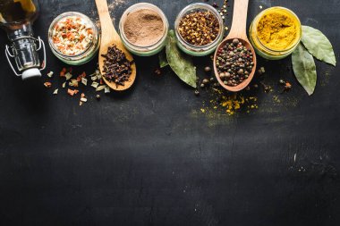 Farklı baharatlar ve siyah arkaplana saçılmış gıda malzemeleri.