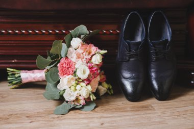 Ahşap arka planda düğün buketi olan damat ayakkabıları.