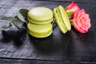 Siyah arka planda çiçeklerle kompozisyonda tatlı renkli badem kurabiyeleri. Boşluğu kopyala