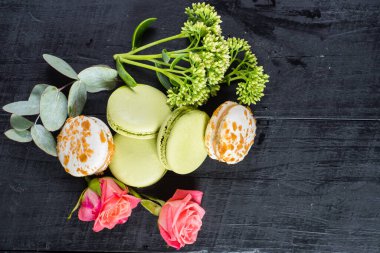 Siyah arka planda çiçeklerle kompozisyonda tatlı renkli badem kurabiyeleri. Boşluğu kopyala