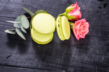 Siyah arka planda çiçeklerle kompozisyonda tatlı renkli badem kurabiyeleri. Boşluğu kopyala