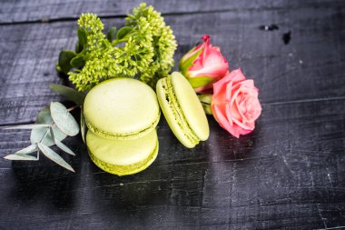 Siyah arka planda çiçeklerle kompozisyonda tatlı renkli badem kurabiyeleri. Boşluğu kopyala