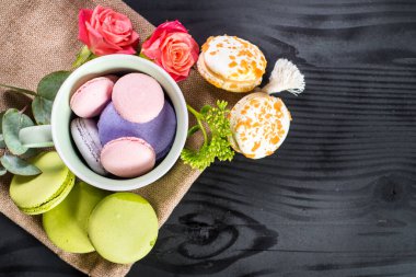 Siyah arka planda çiçeklerle kompozisyonda tatlı renkli badem kurabiyeleri. Boşluğu kopyala