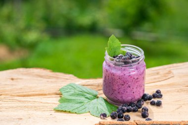 Yeşil bahçe arka planının üzerinde tahta tahtada farklı meyveler içinde tatlı yoğurt.